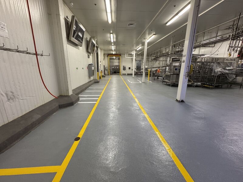 Worker in food processing facility with integrated 5S floor markings showing yellow traffic lanes and orange equipment zone boundaries on resinous flooring system