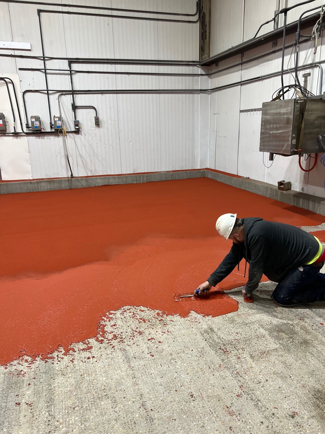 Crew member troweling red SaniCrete SL cementitious urethane in beef plant corner