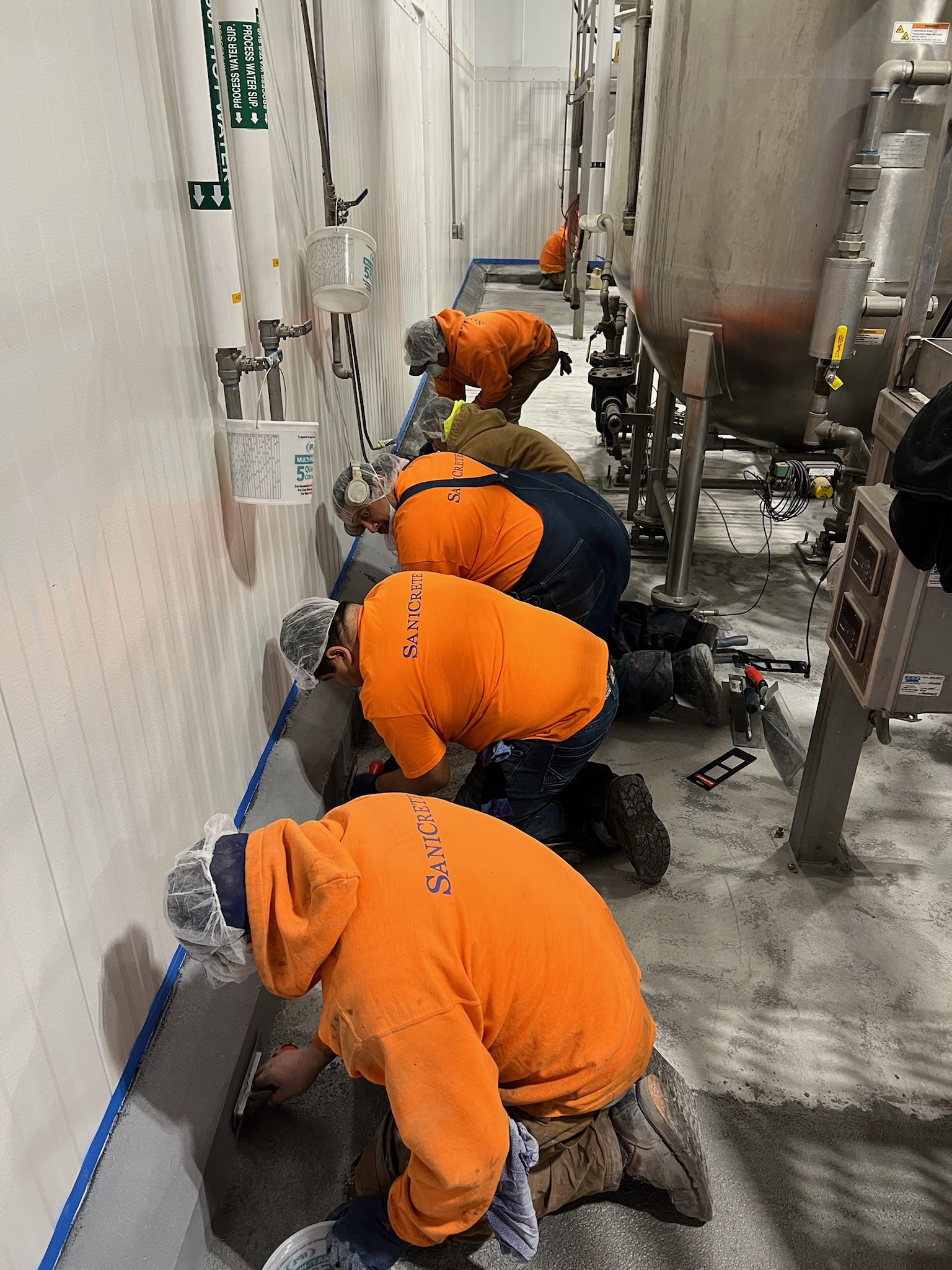 SaniCrete crew in orange hoodies installing cove base at a food processing facility