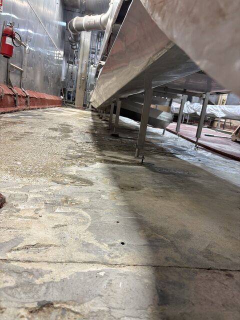 Prepared concrete floor under dairy processing conveyors before SaniBulk slope repair and STX topcoat