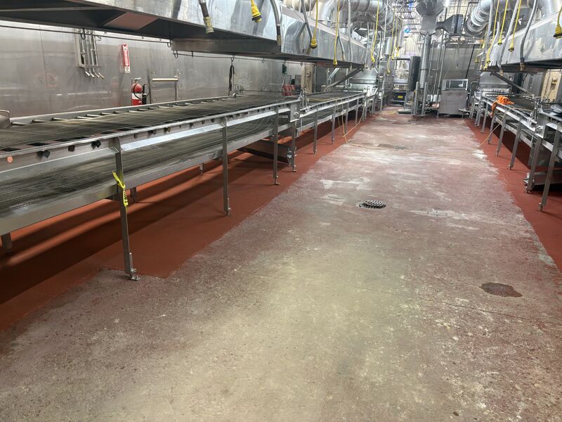 Wide view of completed red SaniCrete STX floor beneath two low-clearance dairy processing conveyor lines