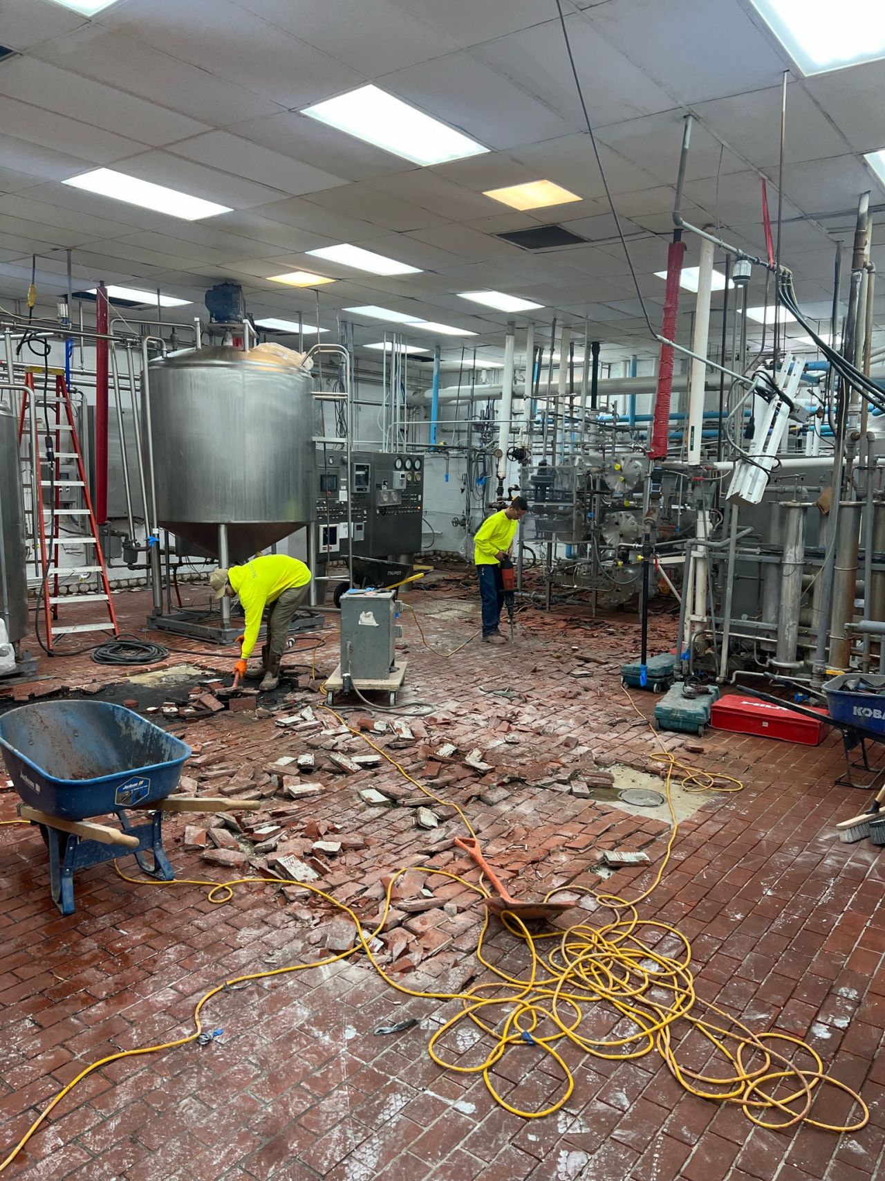 SaniCrete crew removing failing dairy brick from production floor at midwest dairy facility with wheelbarrow and chipping tools