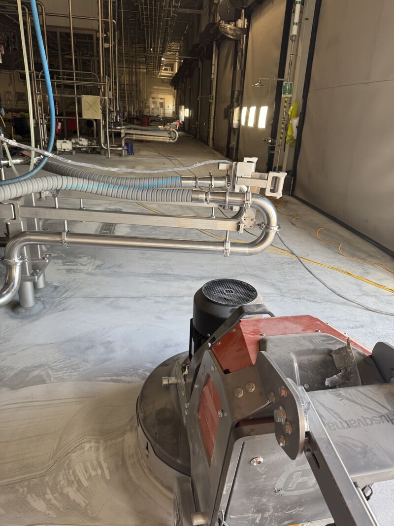 Floor grinder beside stainless process piping during dairy shutdown resurfacing prep