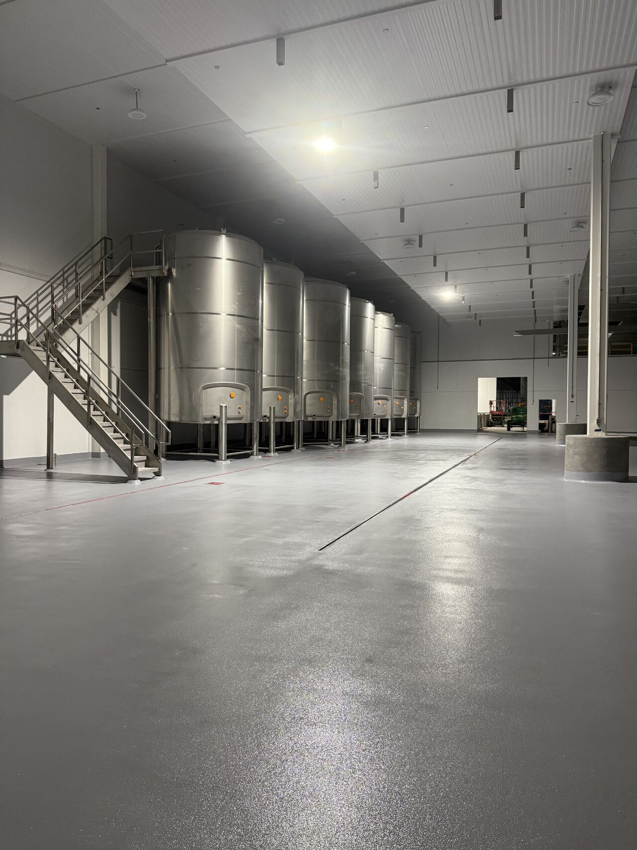 Finished gray dairy floor surrounding stainless steel tanks, stairs, columns, and equipment supports