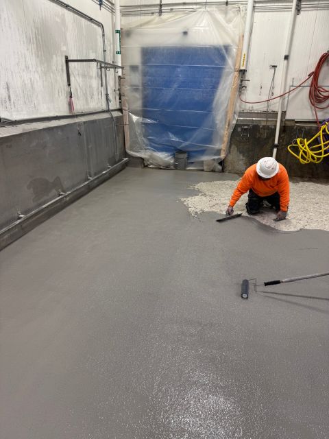 Installer placing and finishing gray SaniCrete STX along the production room wall