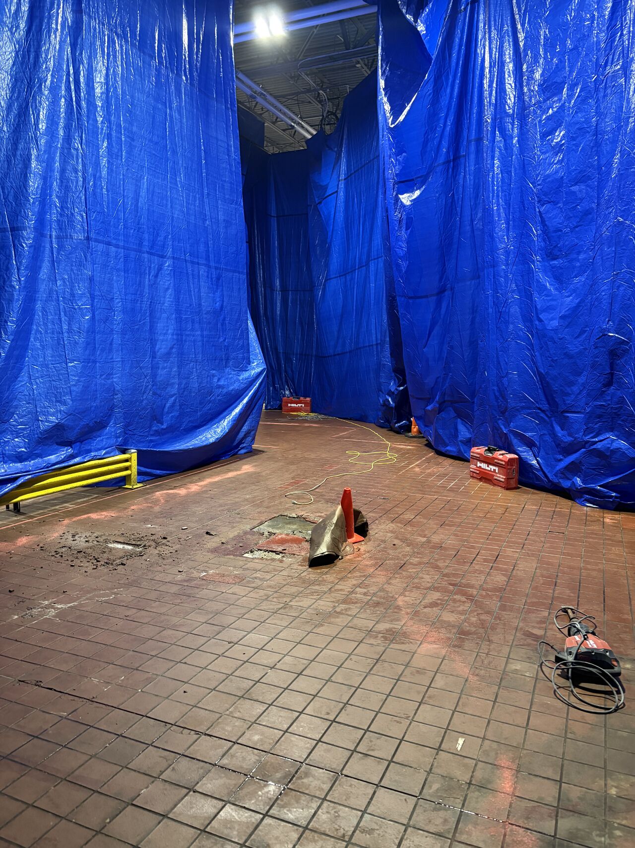 Existing tile floor in a food plant traffic path with damaged tile visible under blue containment tarps