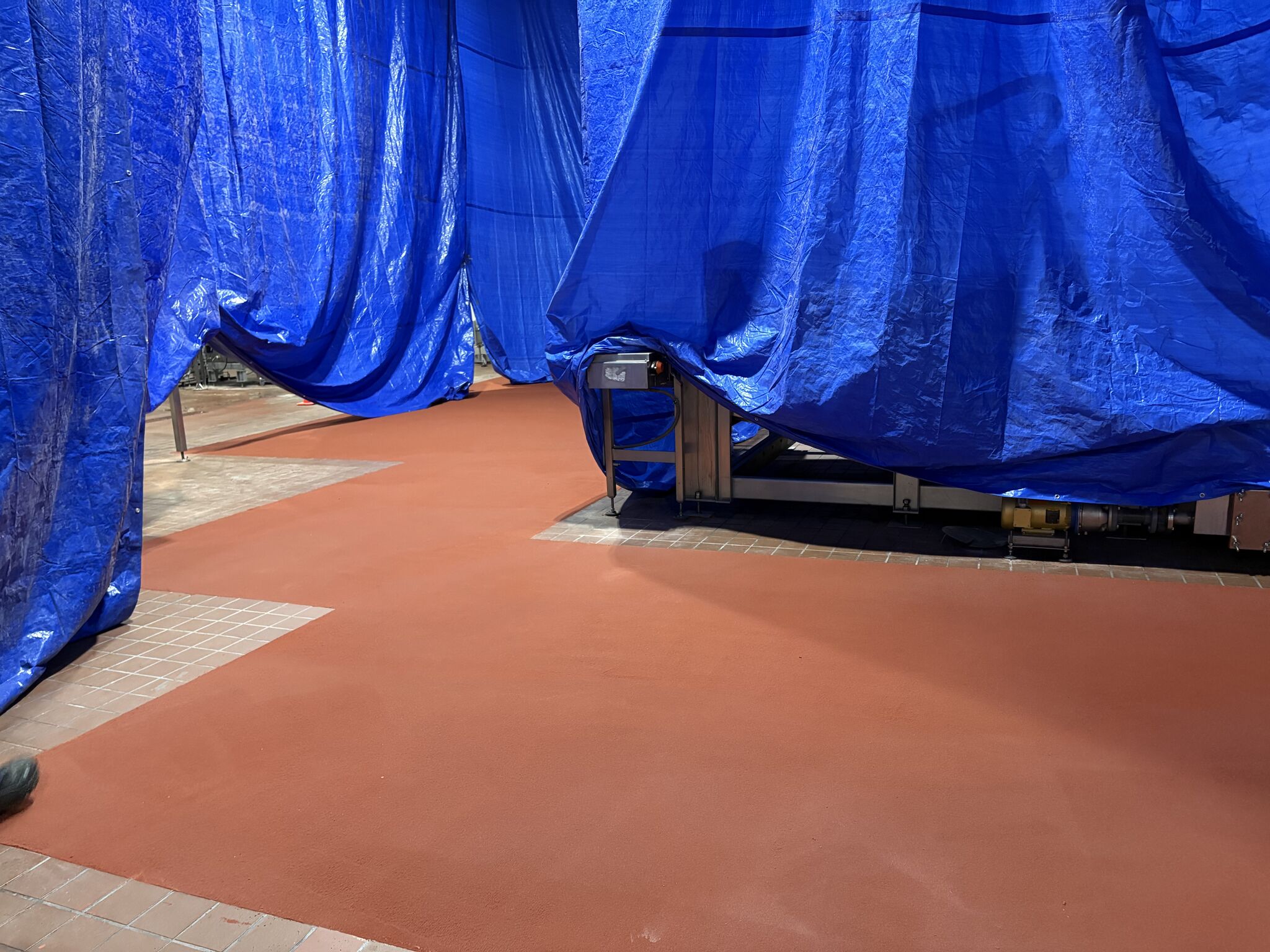 Fresh red SaniCrete STX floor installed around equipment and existing tile in a contained food plant area