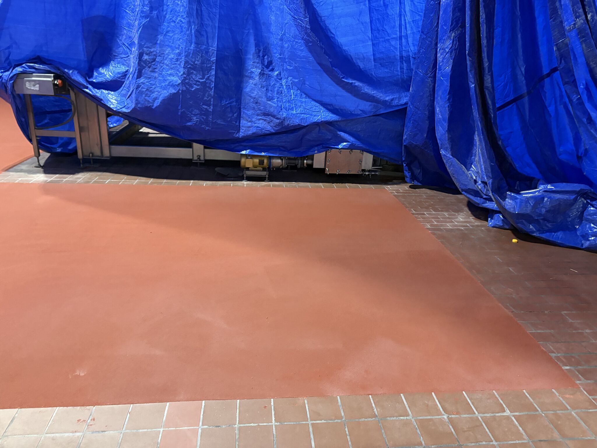 Close view of finished red SaniCrete STX floor beside existing tile and equipment in a food plant