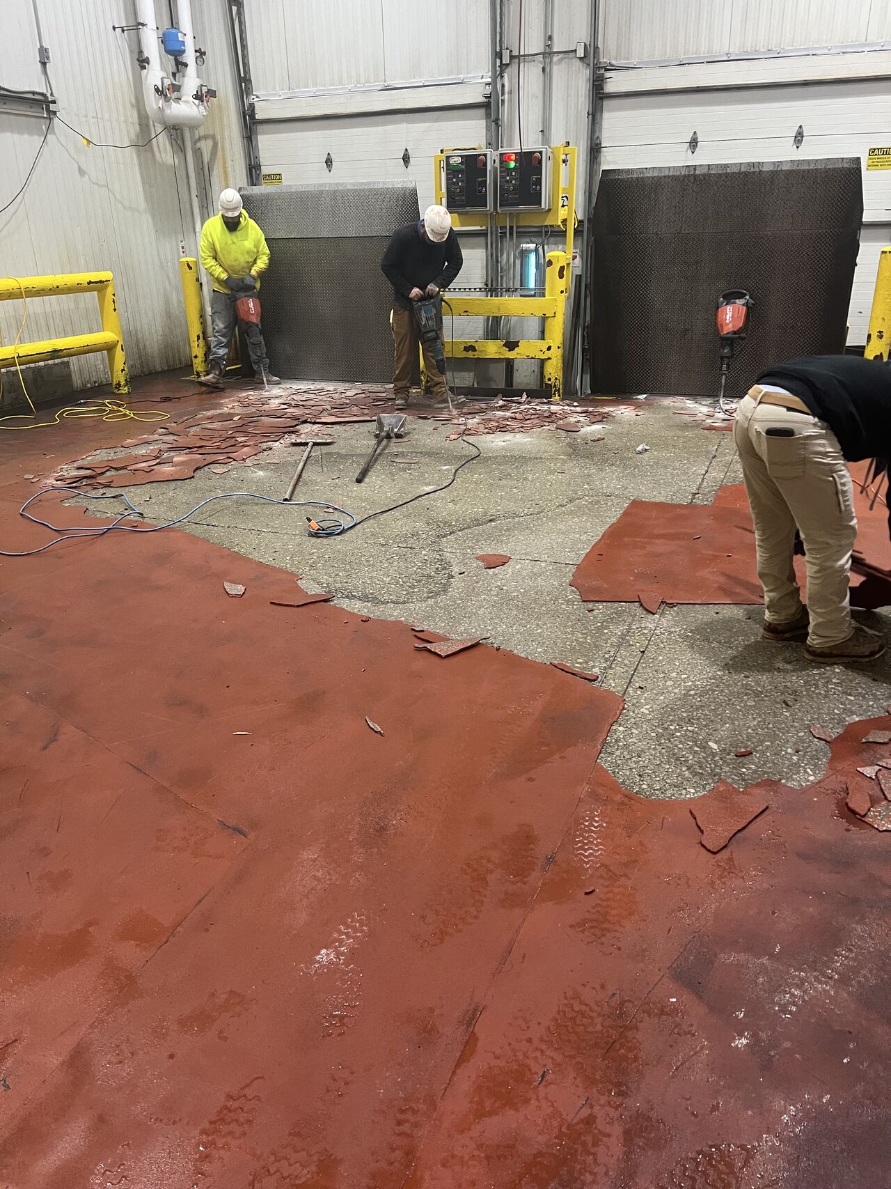 Crew removing badly delaminated red epoxy coating from loading dock floor with chipping hammers