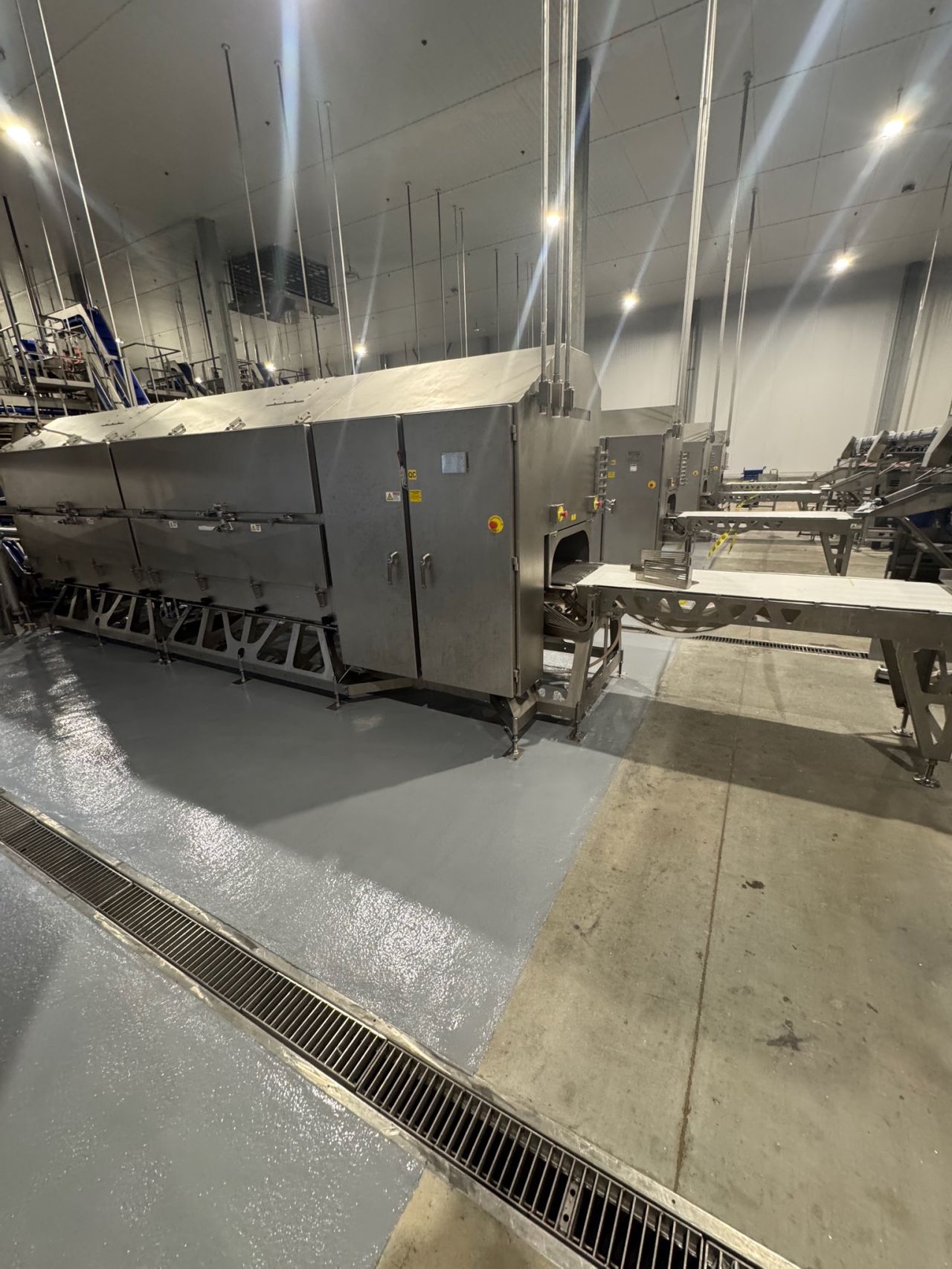 Completed gray SaniCrete STX floor under large processing equipment with trench drain visible