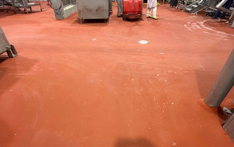 Close view of finished red SaniCrete STX floor around equipment and floor drains in a meat processing room