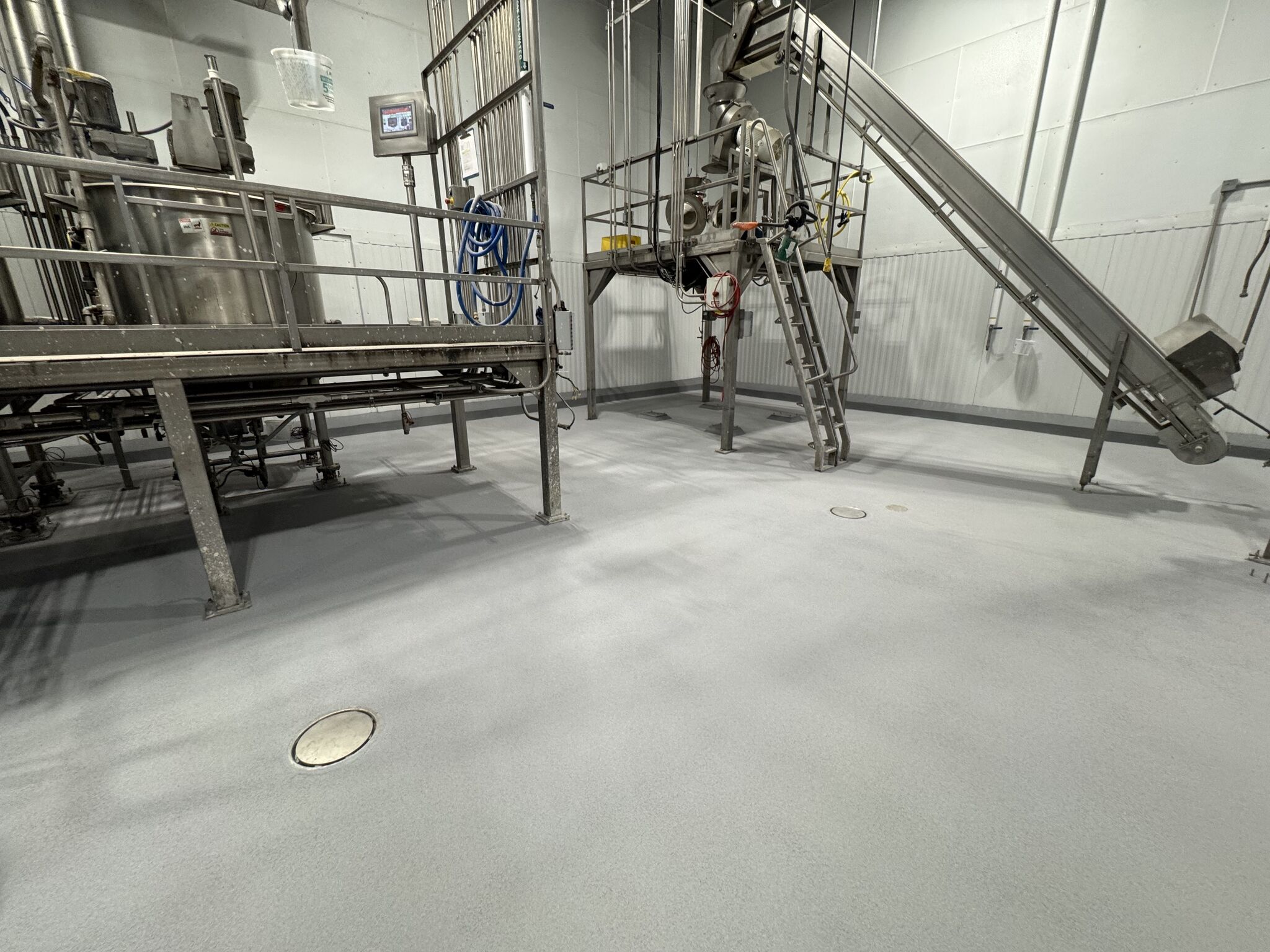 Completed seamless gray SaniCrete STX floor with new spot drains and production equipment in food processing facility