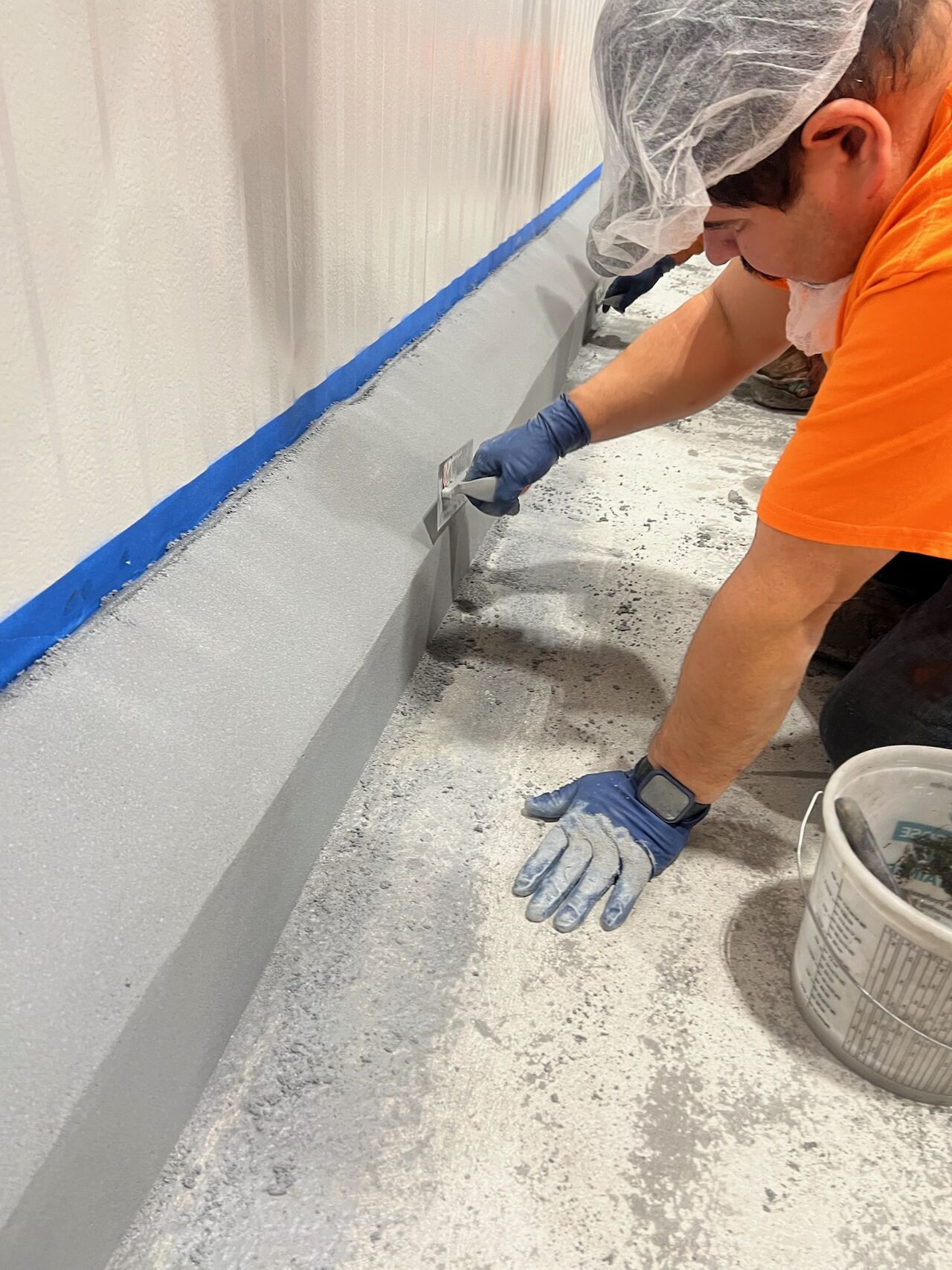 Crew member hand-troweling SaniCrete VR cant cove curbing along wall in food processing facility