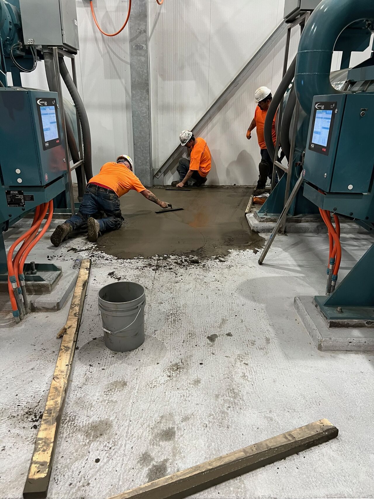 SaniCrete crew in orange shirts troweling SaniBulk polymer concrete between compressors to create proper drainage slope