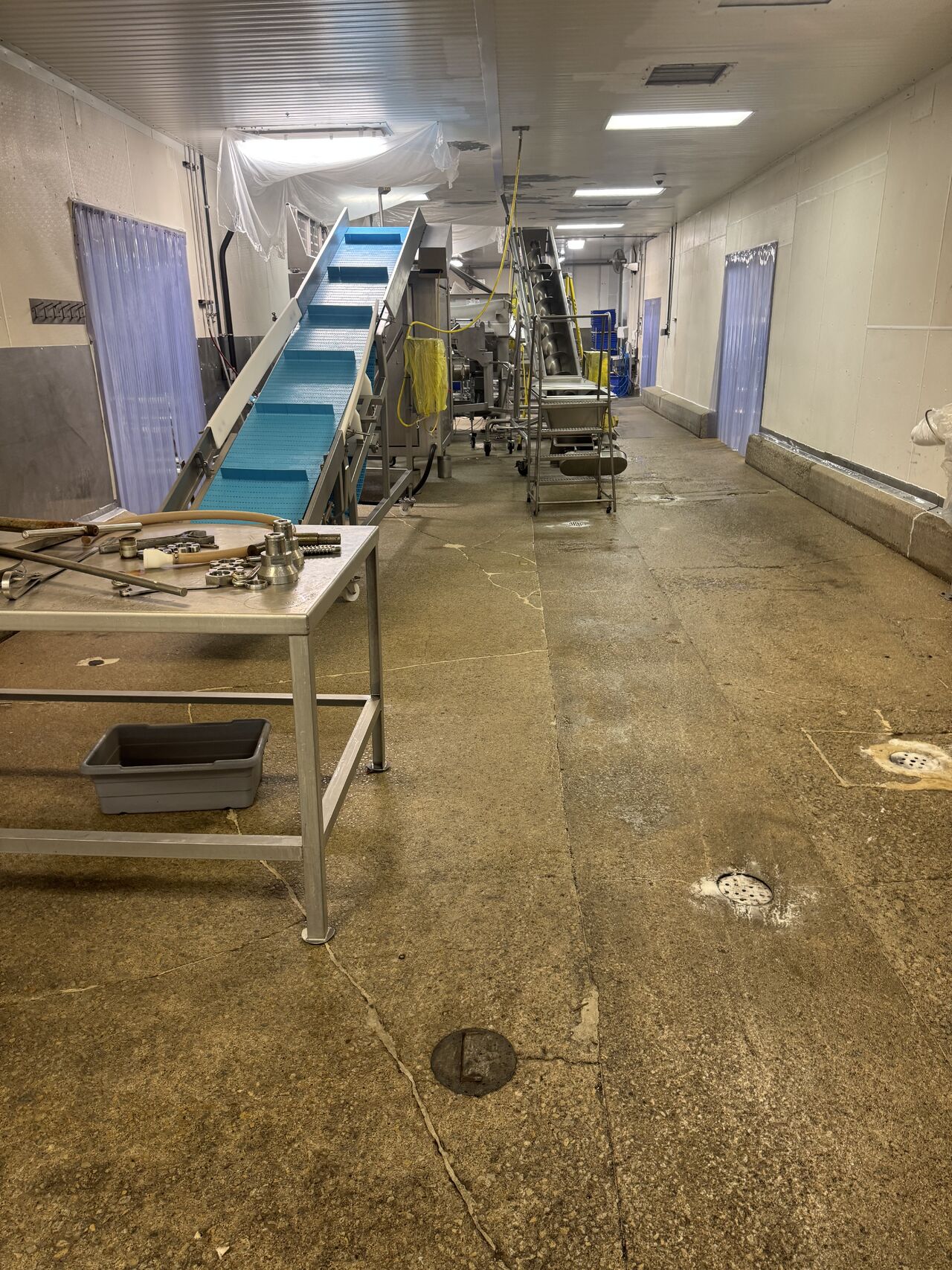 Uncoated concrete floor in processing hallway with conveyor belt before flooring installation