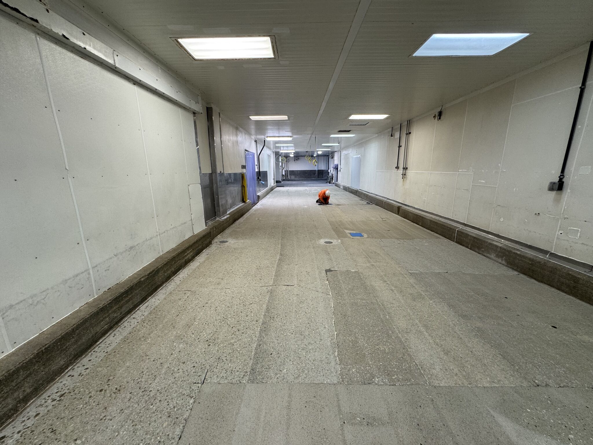 Prepared concrete substrate in oven room hallway with worker detailing edges before topcoat