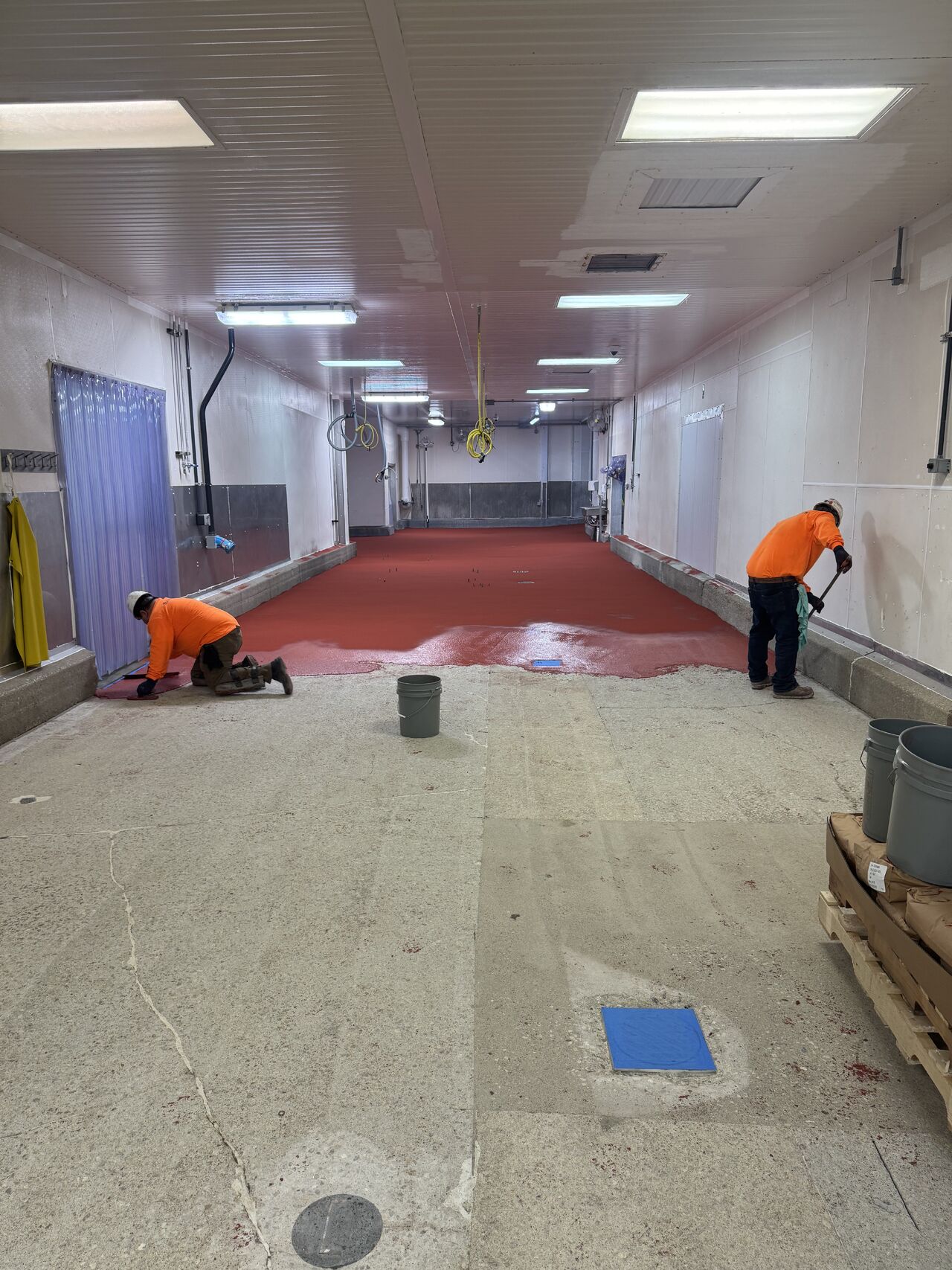 Two SaniCrete installers applying STX flooring showing progress from bare concrete to finished floor