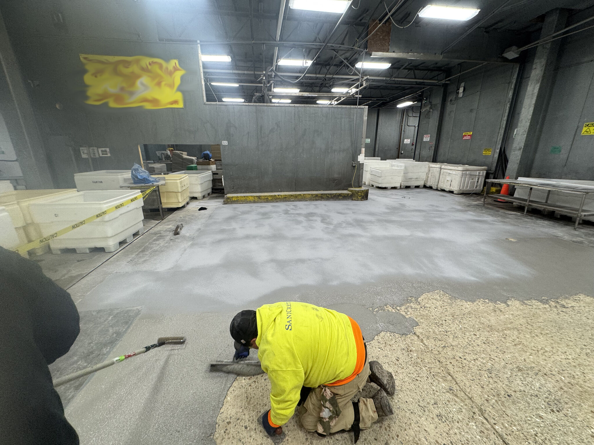 Crew member troweling fresh SaniCrete STX with wet seamless floor visible behind