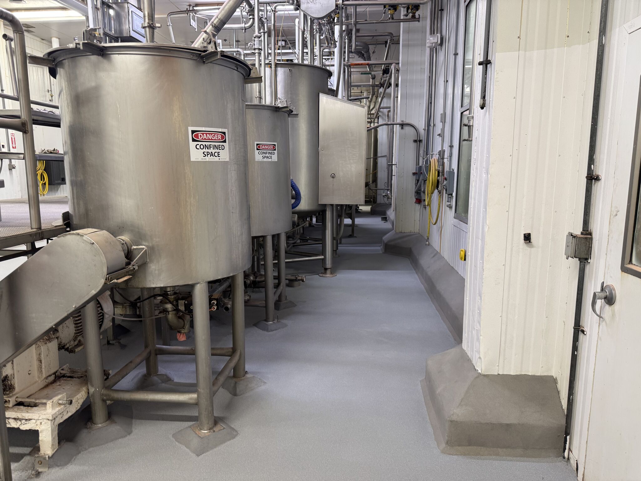 Completed — gray STX floor running past stainless tanks with Danger Confined Space signs and curbing detail