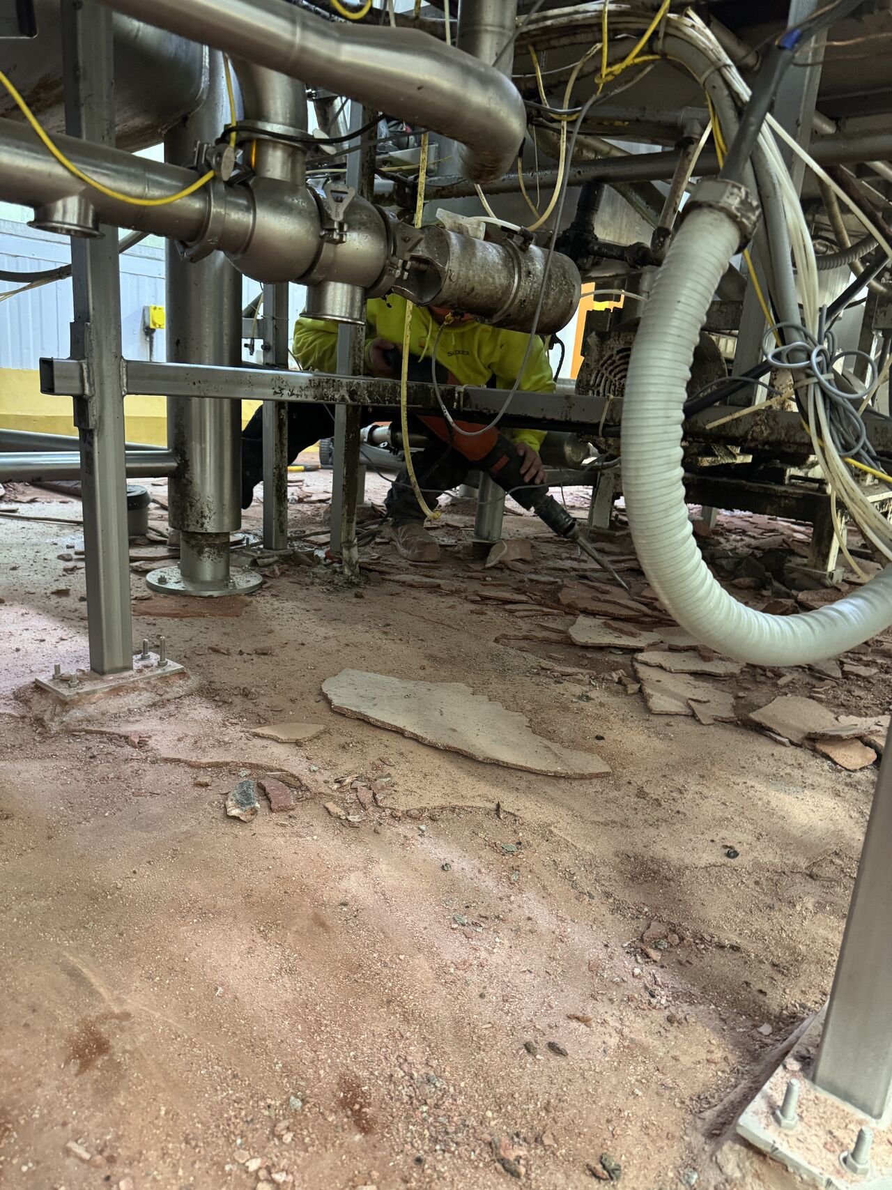 During demolition — crew member working under equipment to remove old flooring down to bare concrete