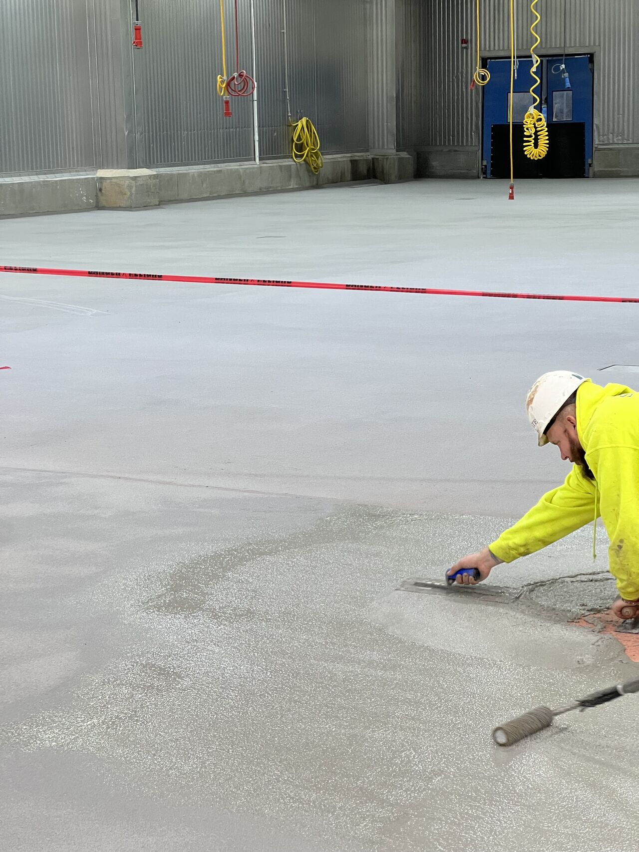 SaniCrete crew member in yellow hi-vis troweling fresh STX cementitious urethane on production floor
