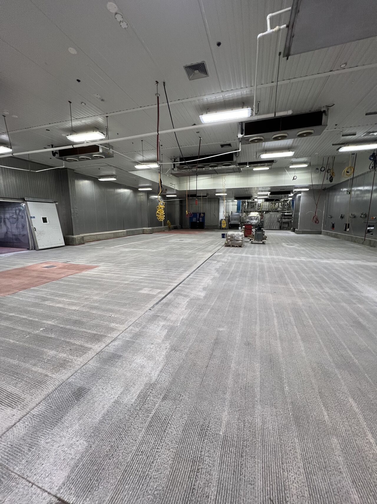 Large production room after scarification — bare concrete with grinding marks, equipment cleared for floor installation
