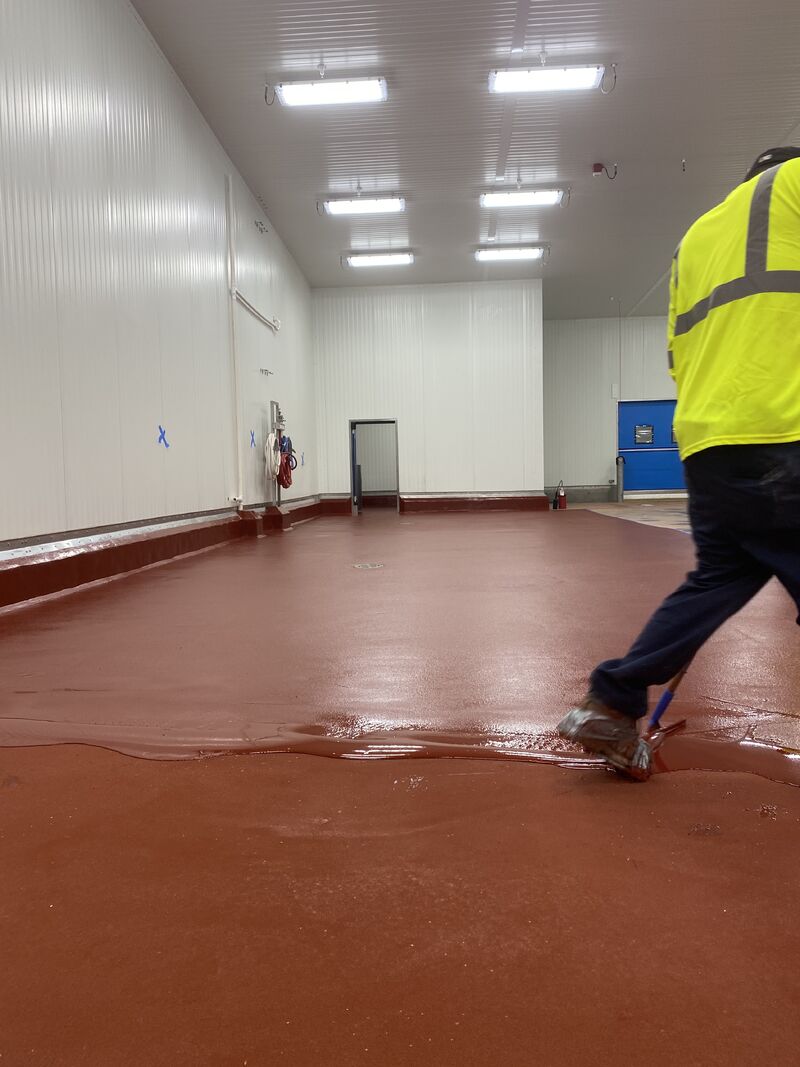 Worker walking on wet red SaniCrete STX floor with aggregate texture for slip resistance