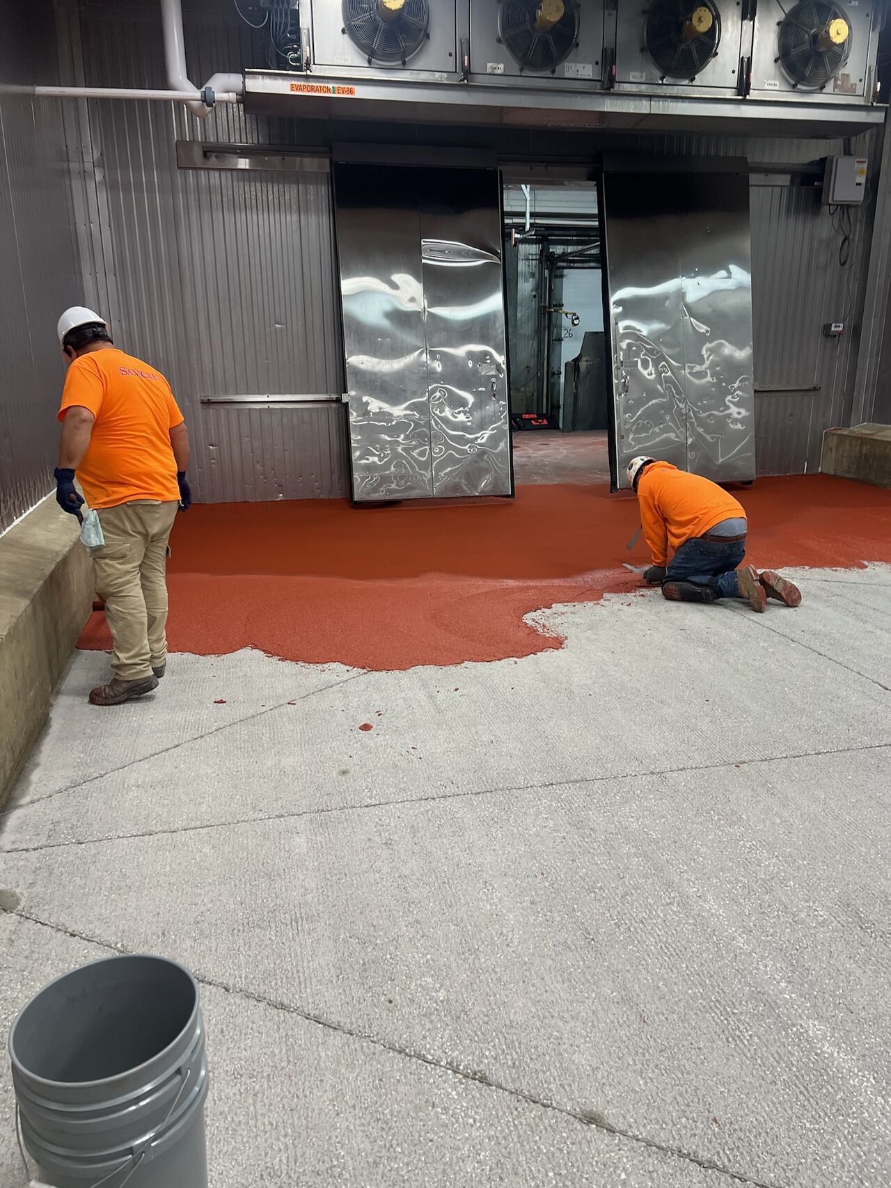 Two SaniCrete crew members installing red-orange STX cementitious urethane in cold storage room