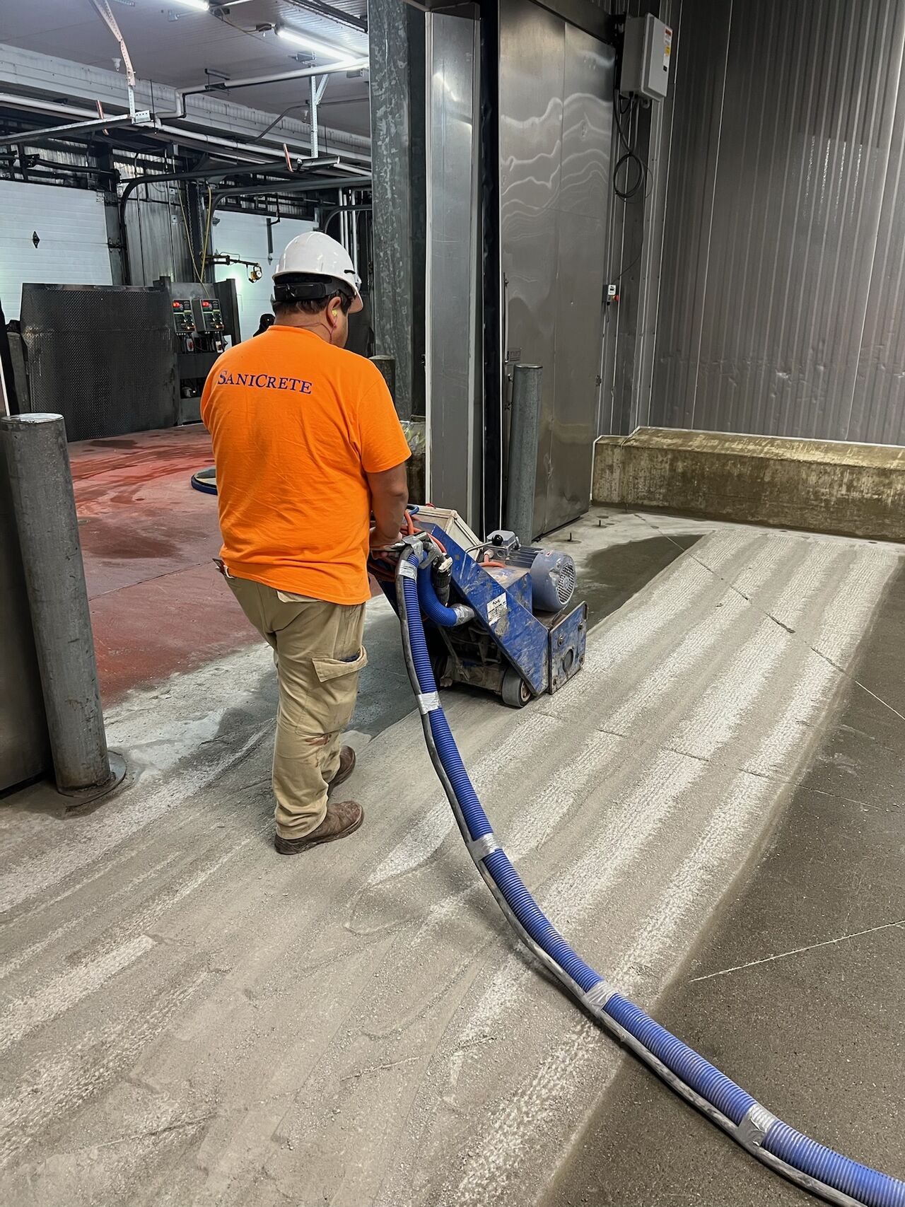 SaniCrete crew member in orange shirt scarifying concrete substrate in cold storage area