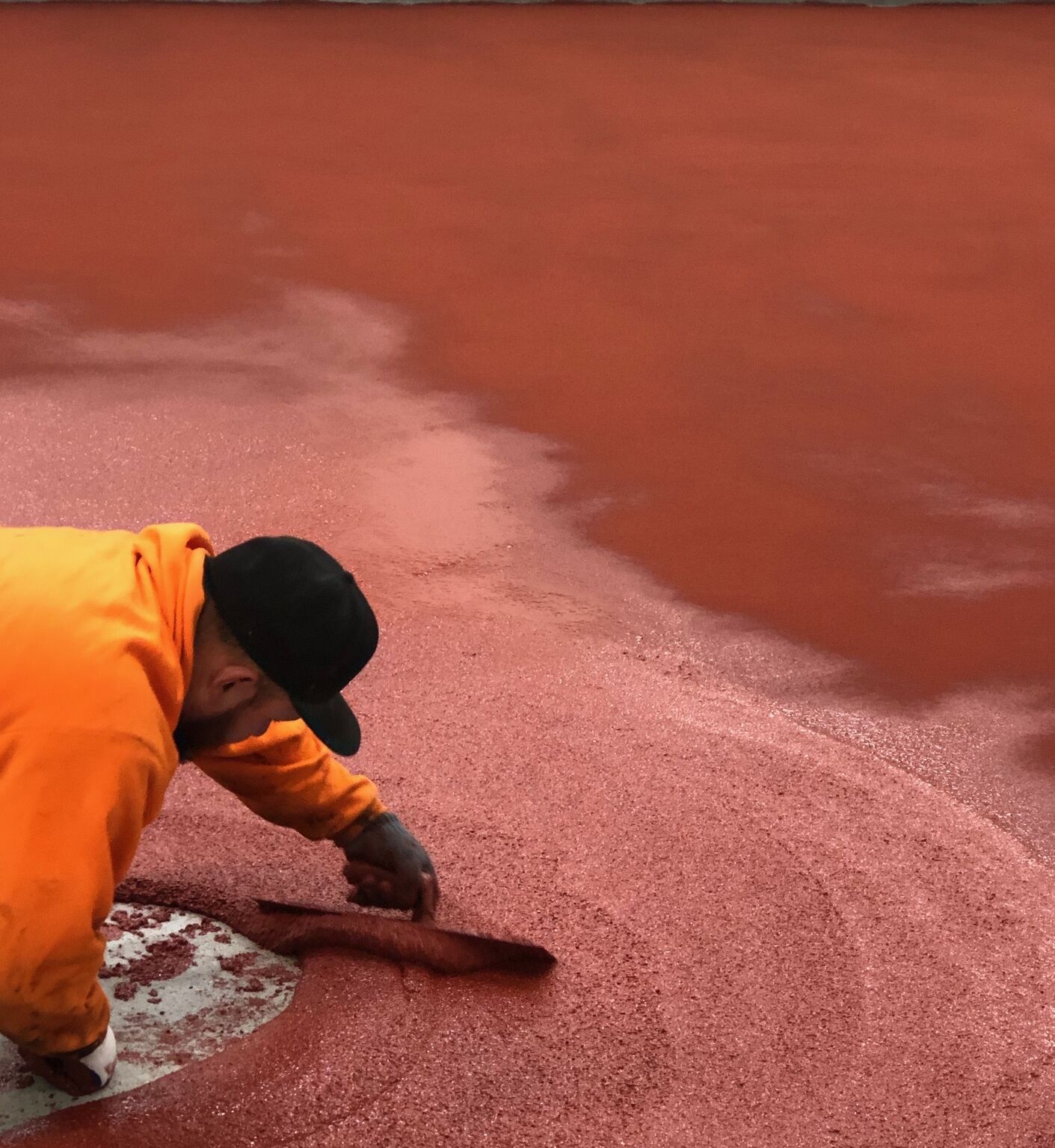 Crew member hand-troweling red STX cementitious urethane around floor drain