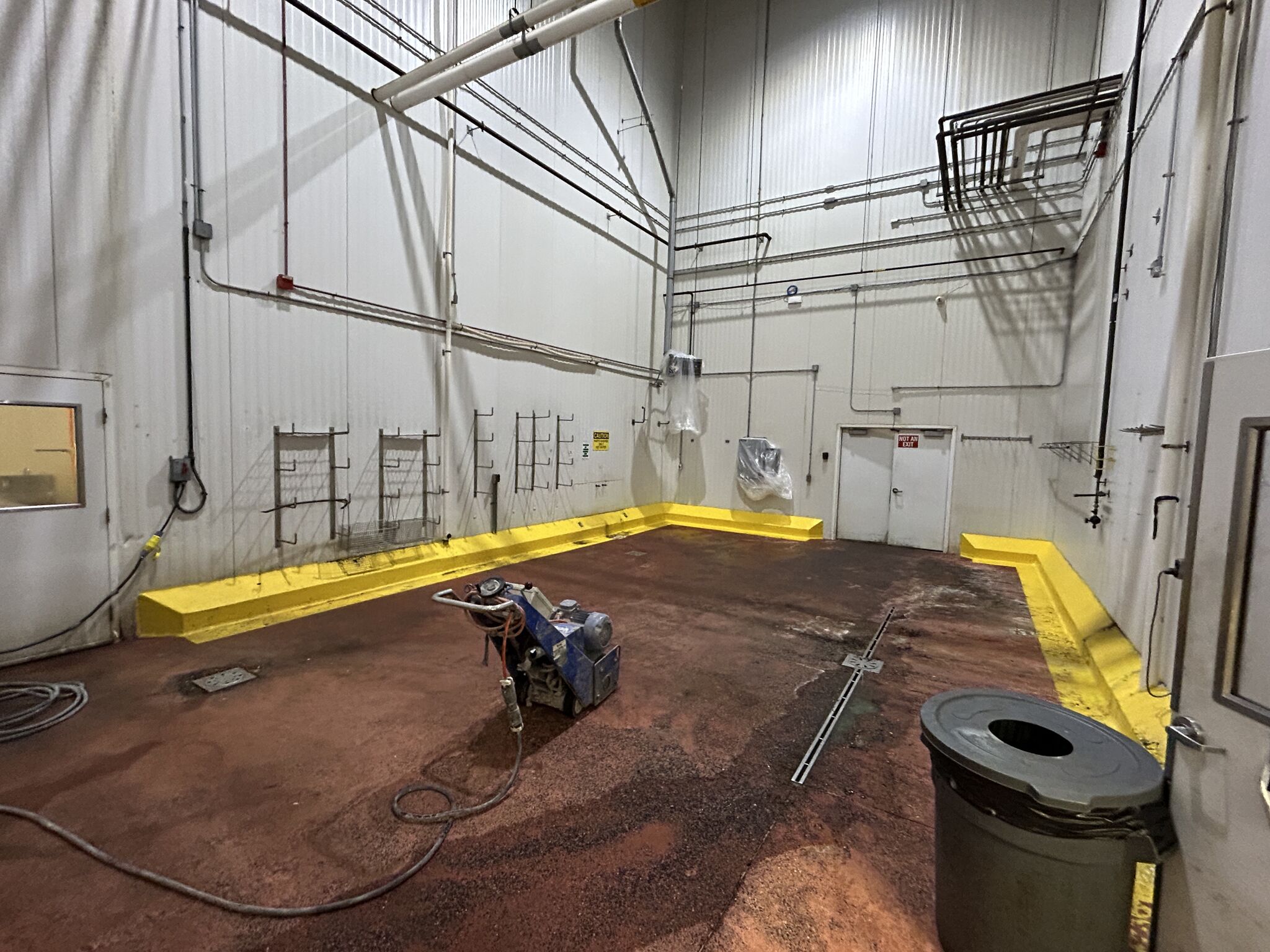 Chemical room before renovation — deteriorating red-brown floor with yellow curbing and grinding equipment