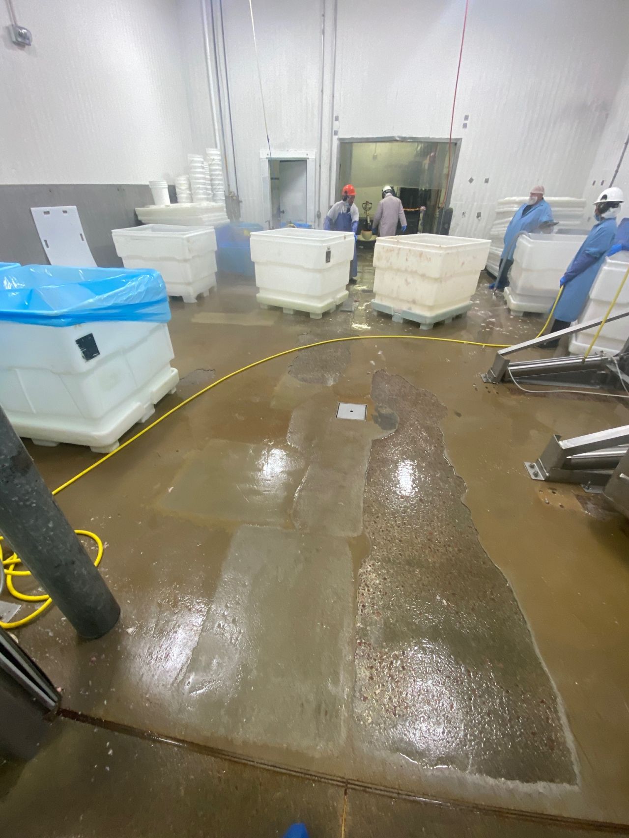 Poultry processing washdown area before — severely deteriorated floor with standing water, exposed concrete, and workers in protective gear